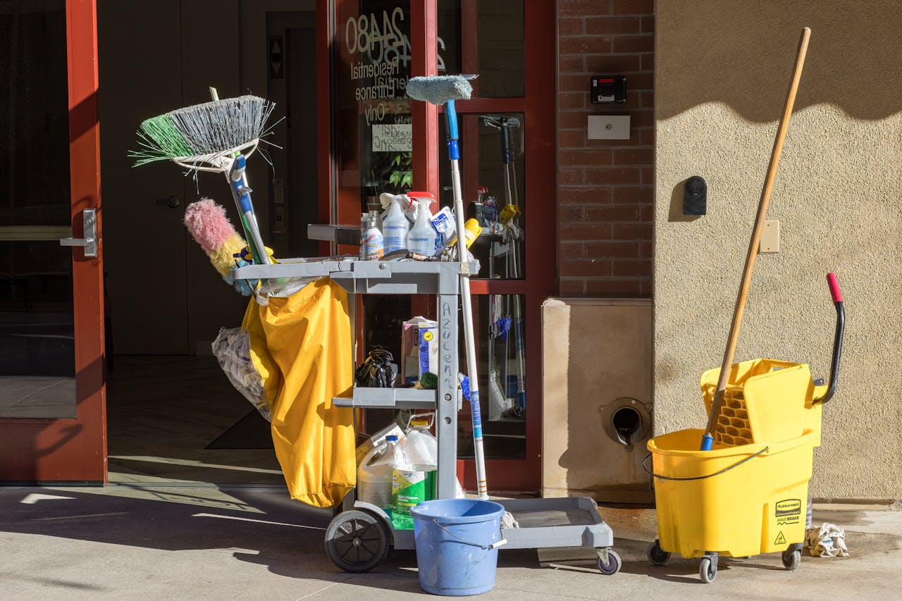 Cleaning supplies and tools outside a building entrance bathed in sunlight.