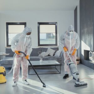 Two workers in protective gear vacuum and disinfect a modern living room.