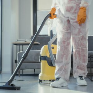 A cleaner in protective coveralls and gloves vacuuming a modern living room.