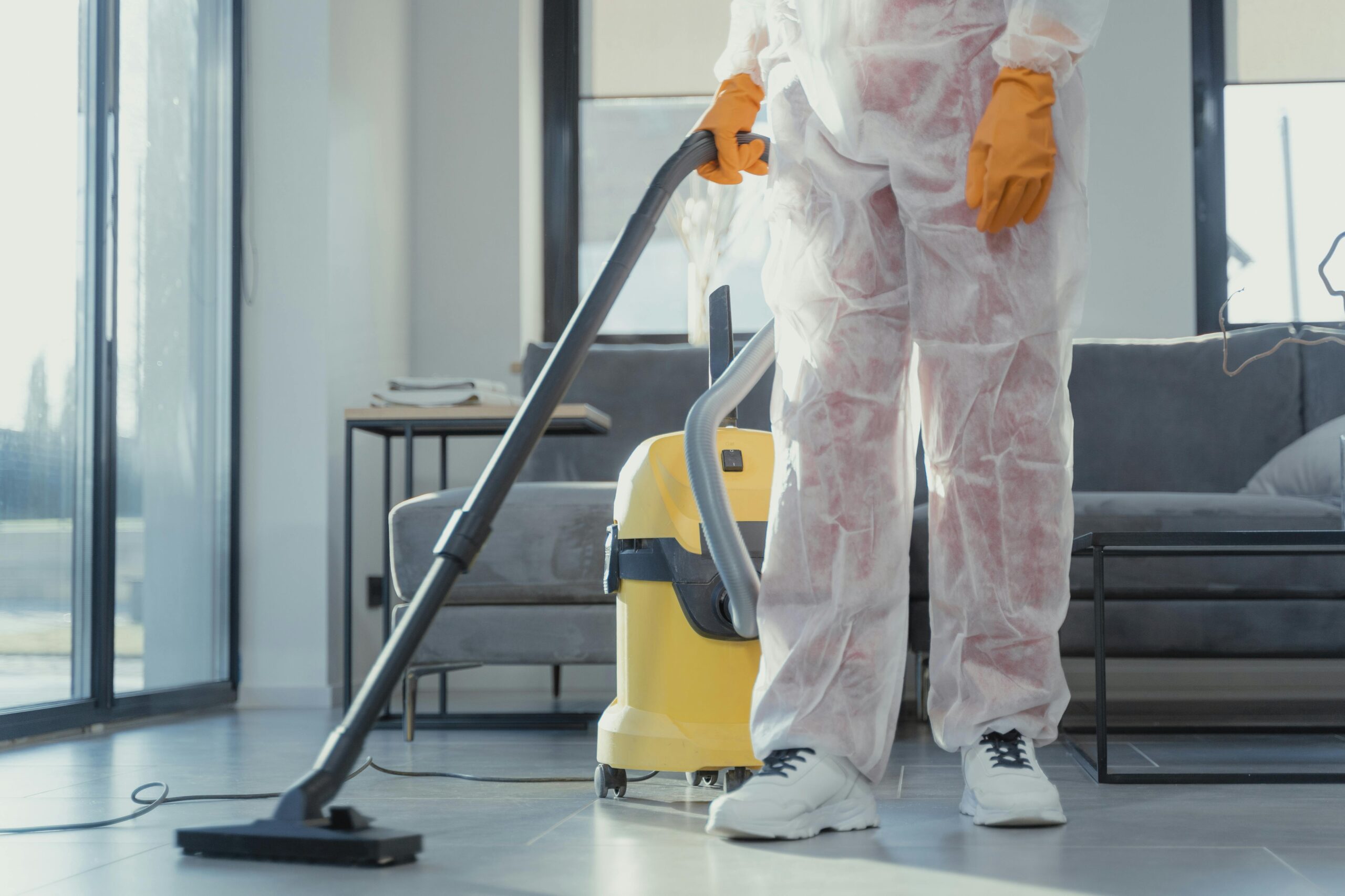 pexels photo 6195951 6195951 A cleaner in protective coveralls and gloves vacuuming a modern living room.